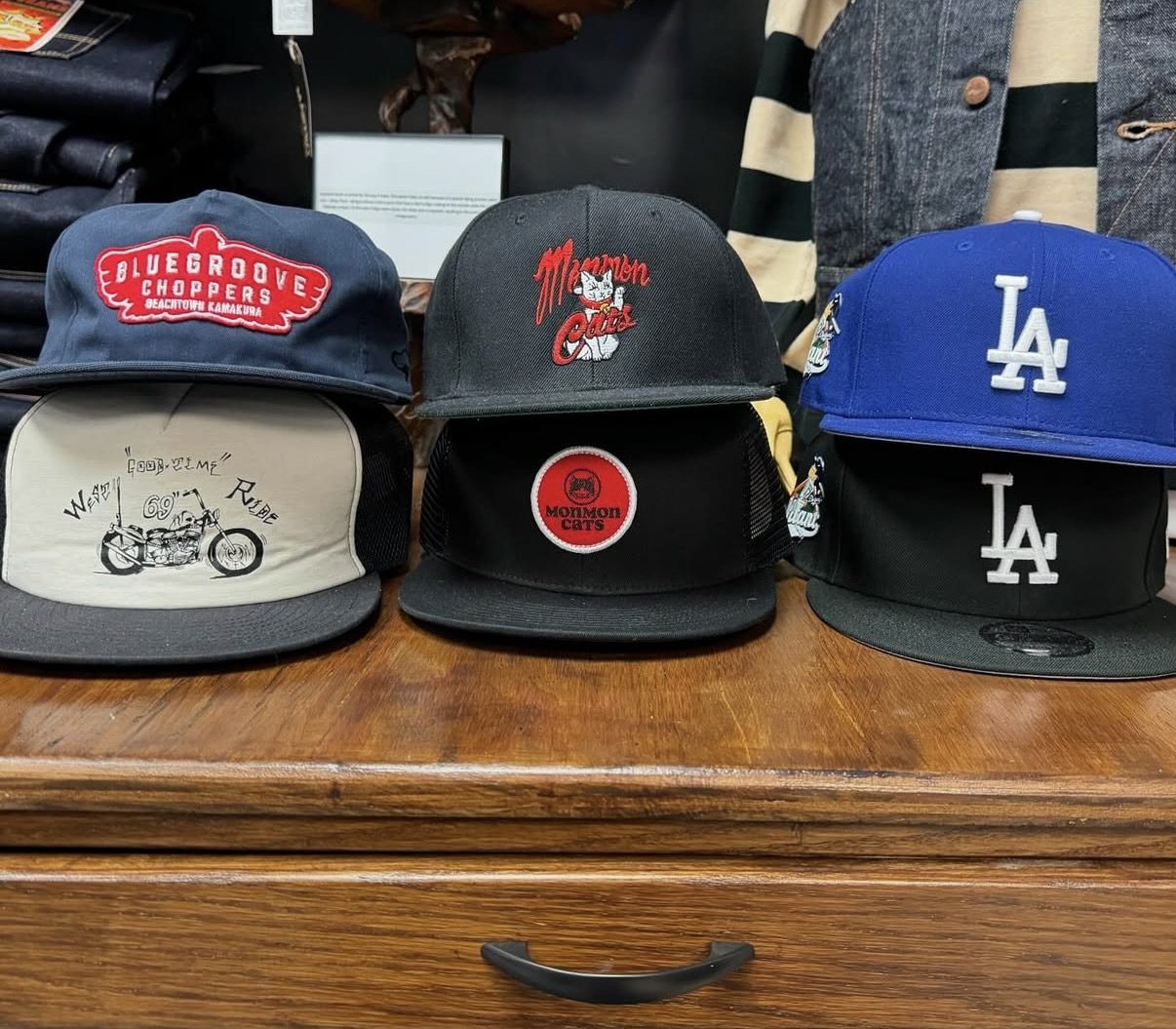 Caps on the shop counter — Blue Groove Choppers from Kamakura, Monmon Cats, and LA fitteds